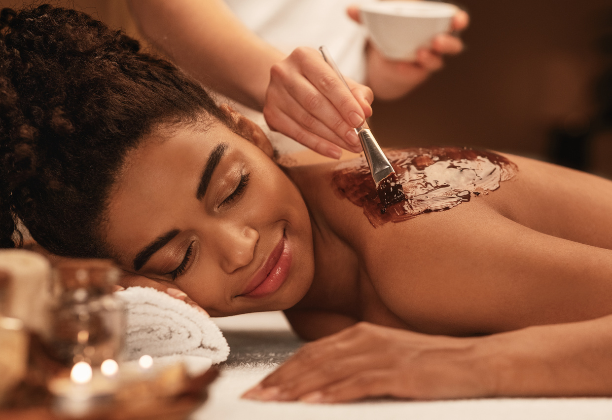 Young black woman receiving body scrub treatment at luxury spa